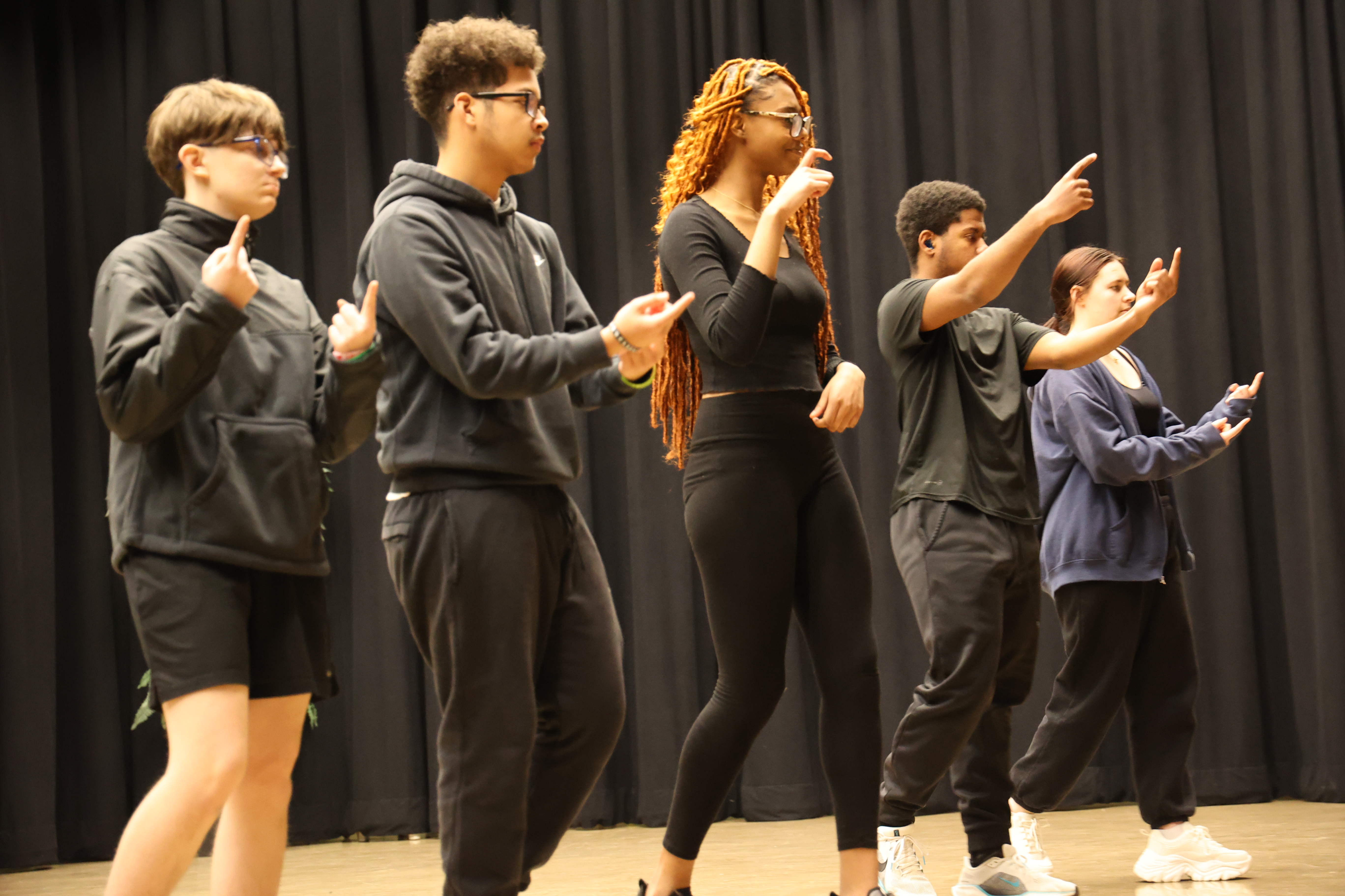 Five students walk forward on a stage while signing in ASL during a performance.