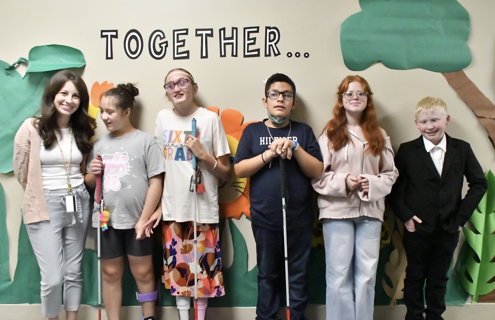 A teacher stands next to five students smiling and posing beneath a sign on the wall that reads 