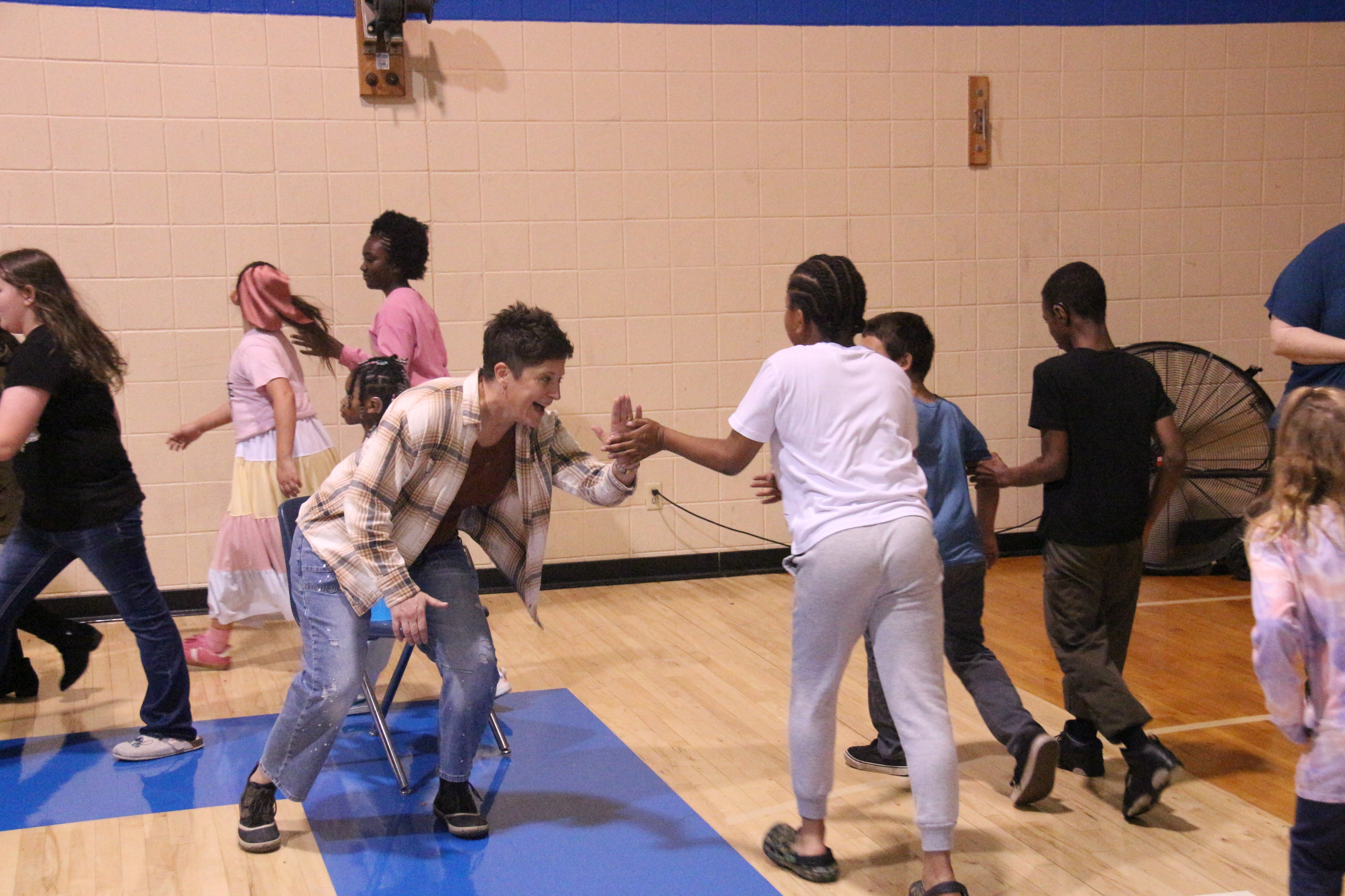 Students are walking in a gym while one of them high-fives an excited educator.